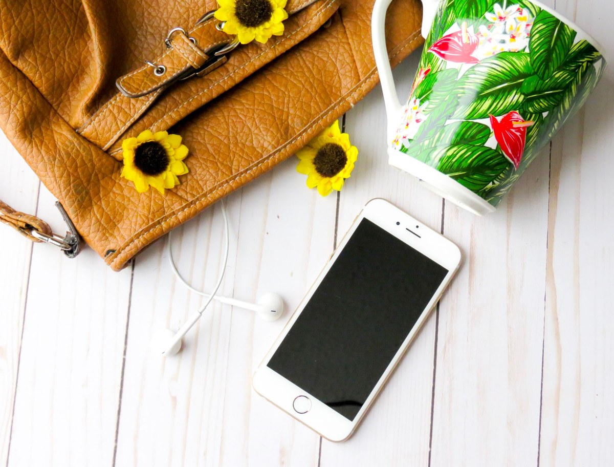 iPhone auf einem hellen weissen Tisch mit Sonnenblumen und einer Tasche