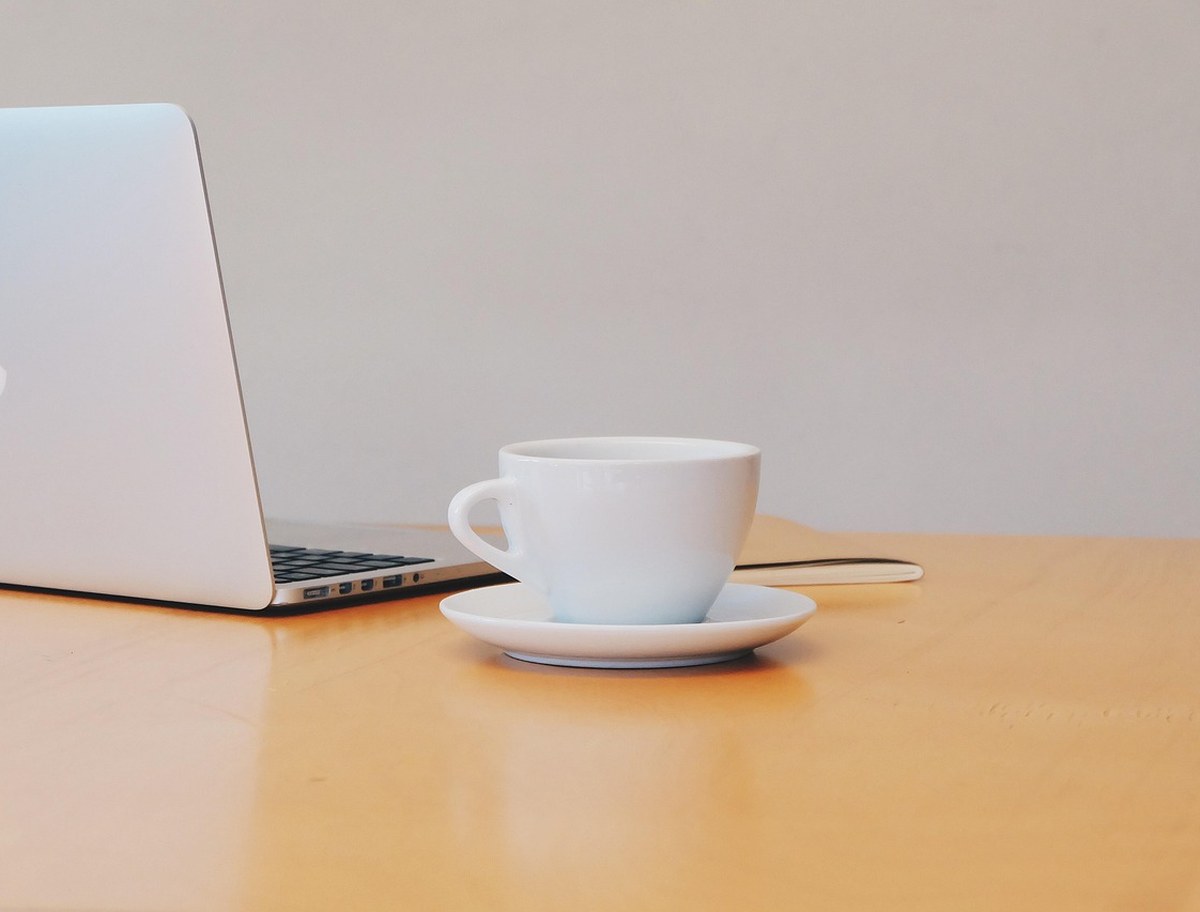 MacBook und weisse Kaffeetasse auf einem warmen hellen Schreibtisch